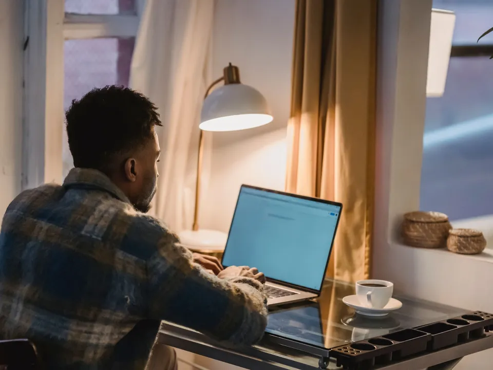 Man werkt 's avonds thuis aan een laptop naast een bureaulamp en koffie